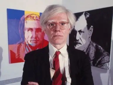 Andy Warhol standing in front of his artworks