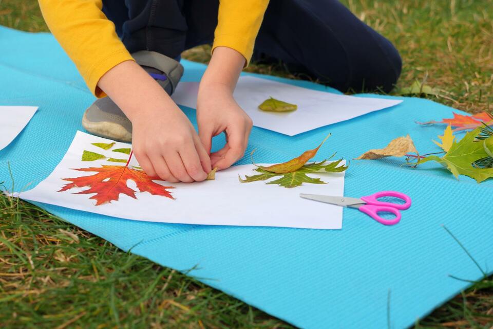 child creating kids art with leaves and paper